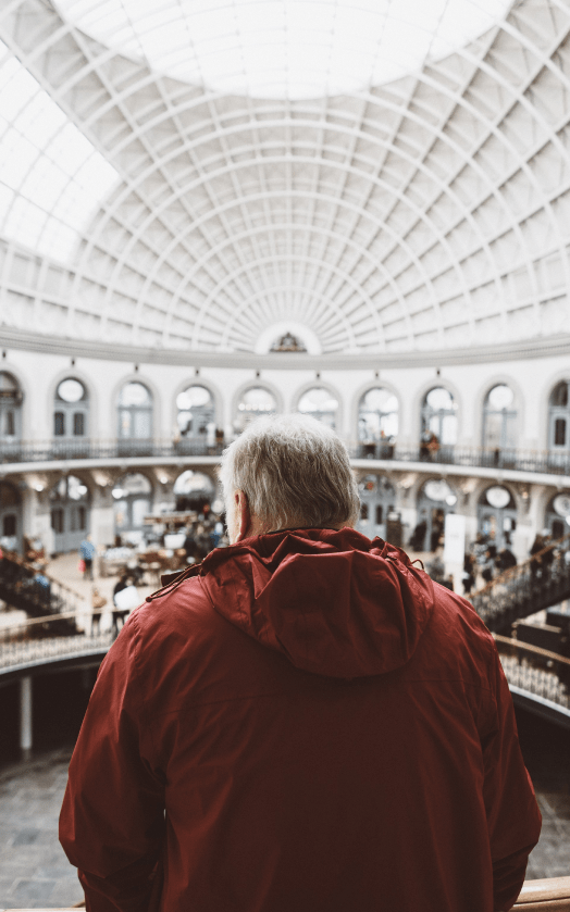 A man in a red jacket observing the grand architecture of a museum's main hall.