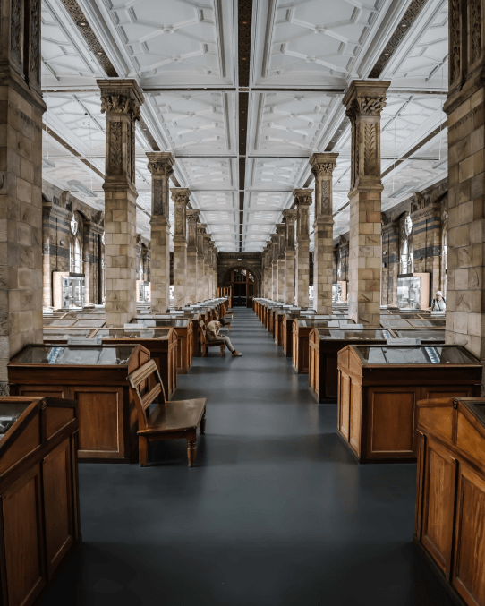 A long, stately hallway with display cases on either side in a historical museum setting.